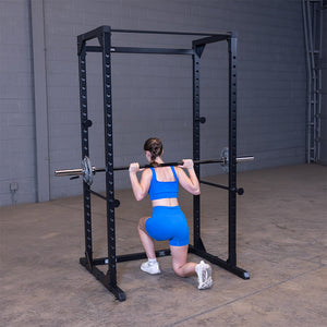 Woman doing a barbell reverse lunge inside the black Best Fitness BFPR100B power rack, rear view